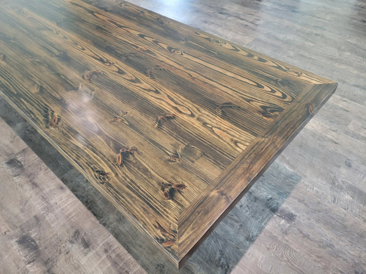 A large rectangular wooden dining table with a glossy dark brown finish and prominent wood grain, shown in a modern kitchen setting with wood-look floors and dark cabinetry.