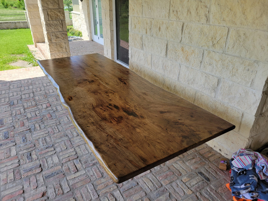 A rustic live-edge Pecan dining table with a natural wood top and black metal X-style legs,