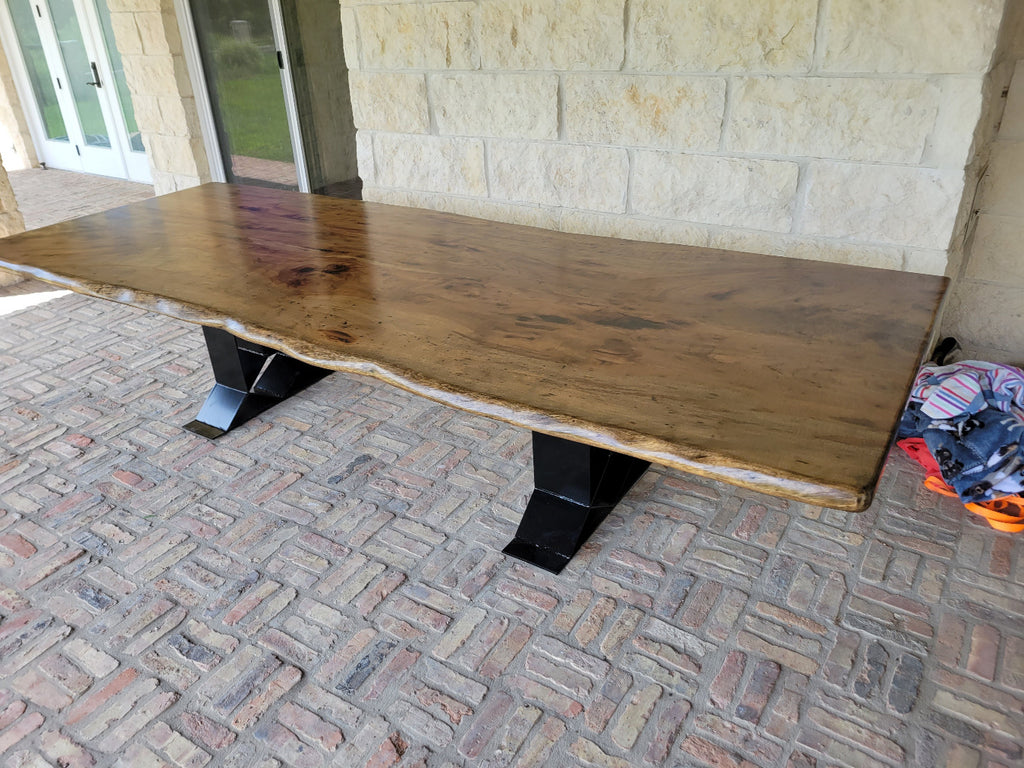 A rustic live-edge Pecan dining table with a natural wood top and black metal X-style legs,