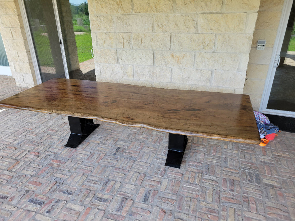A rustic live-edge Pecan dining table with a natural wood top and black metal X-style legs,
