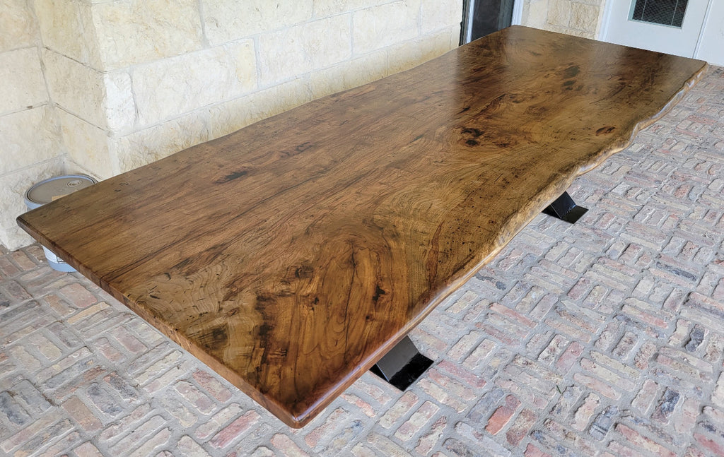 A rustic live-edge Pecan dining table with a natural wood top and black metal X-style legs,