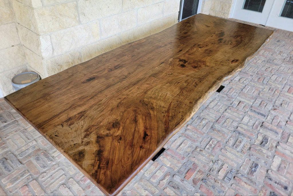 A rustic live-edge Pecan dining table with a natural wood top and black metal X-style legs,
