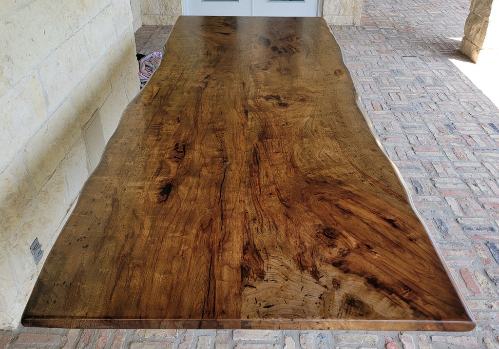 A rustic live-edge Pecan dining table with a natural wood top and black metal X-style legs,
