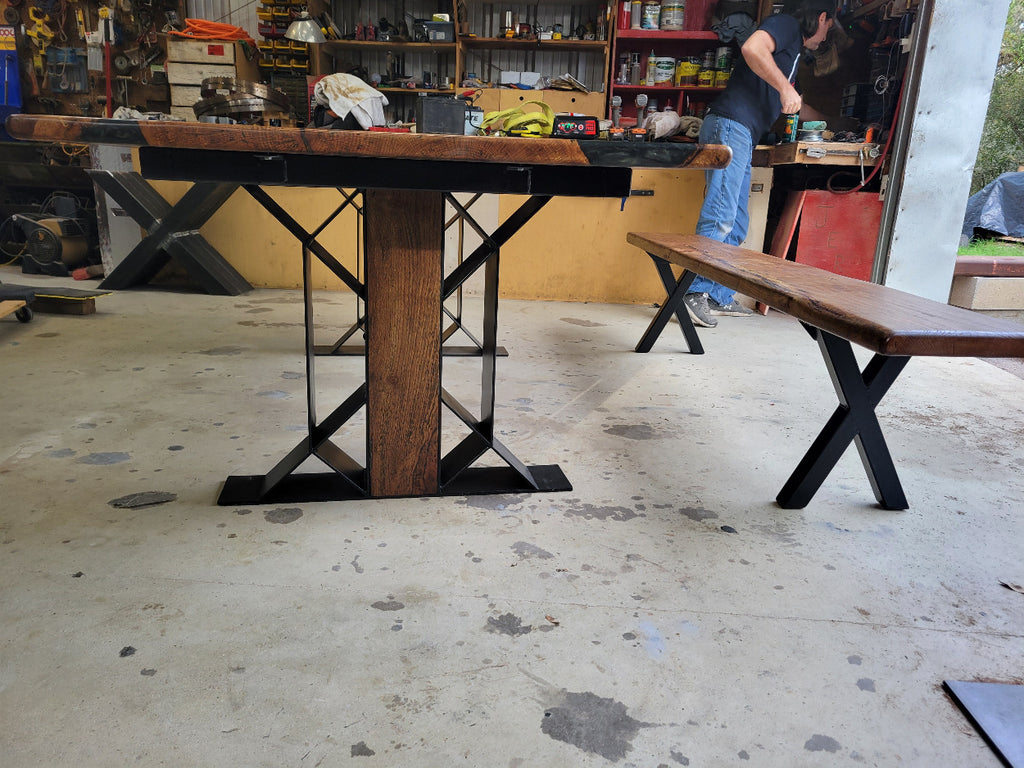 White oak dining table with a natural finish and black resin inclusions with matching bench showing geometric designed metal legs with wood insert