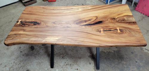 Single slab Hickory dining table with epoxy-filled checks, bow-tie inlays, natural wood finish, and custom metal legs handcrafted by Coleto Creek Mill & Design