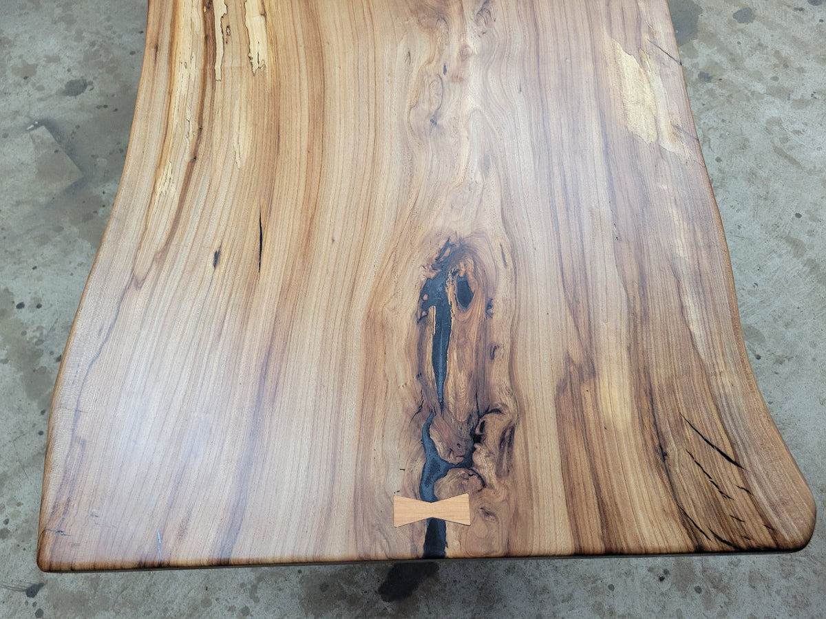 Single slab Hickory dining table with epoxy-filled checks, bow-tie inlays, natural wood finish, and custom metal legs handcrafted by Coleto Creek Mill & Design