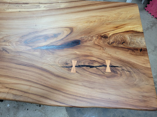 Single slab Hickory dining table with epoxy-filled checks, bow-tie inlays, natural wood finish, and custom metal legs handcrafted by Coleto Creek Mill & Design
