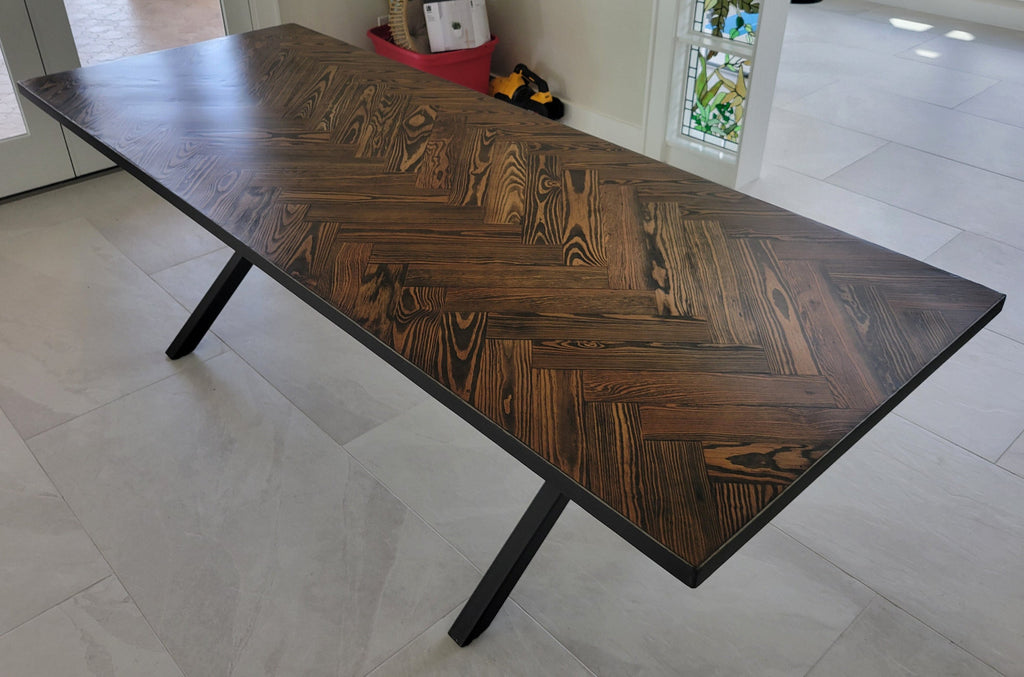 A rectangular long leaf pine dining table with a dark brown herringbone pattern top and black metal legs and metal sides shown in a home interior setting.