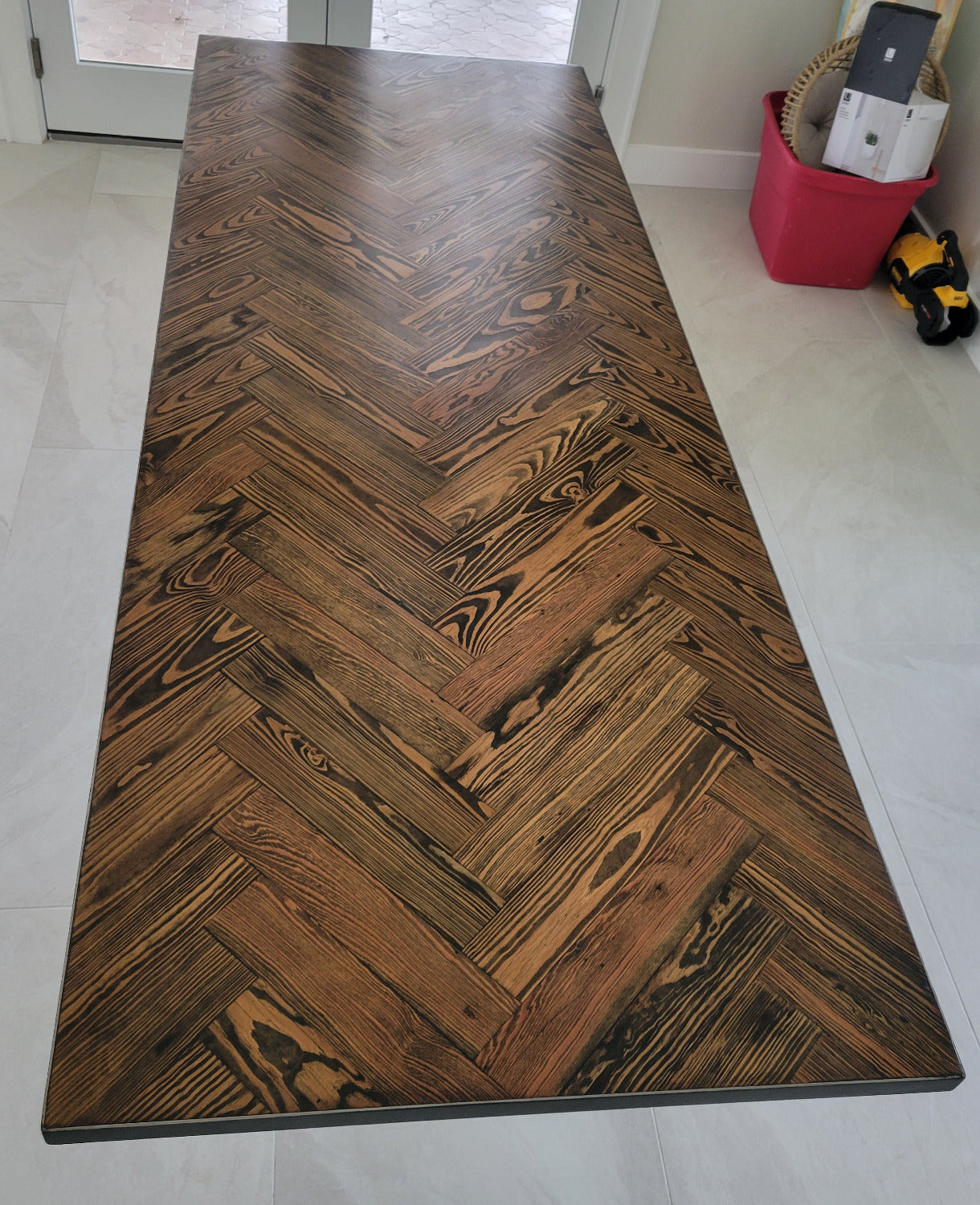 A rectangular long leaf pine dining table with a dark brown herringbone pattern top and black metal legs and metal sides shown in a home interior setting.