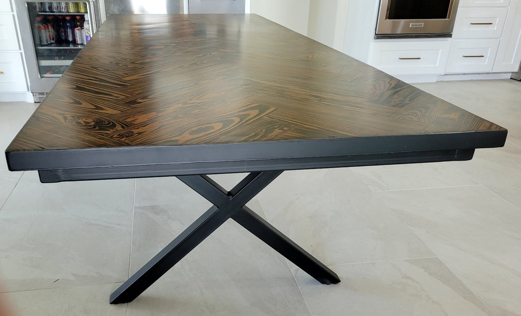 A rectangular long leaf pine dining table with a dark brown herringbone pattern top and black metal legs and metal sides shown in a home interior setting.