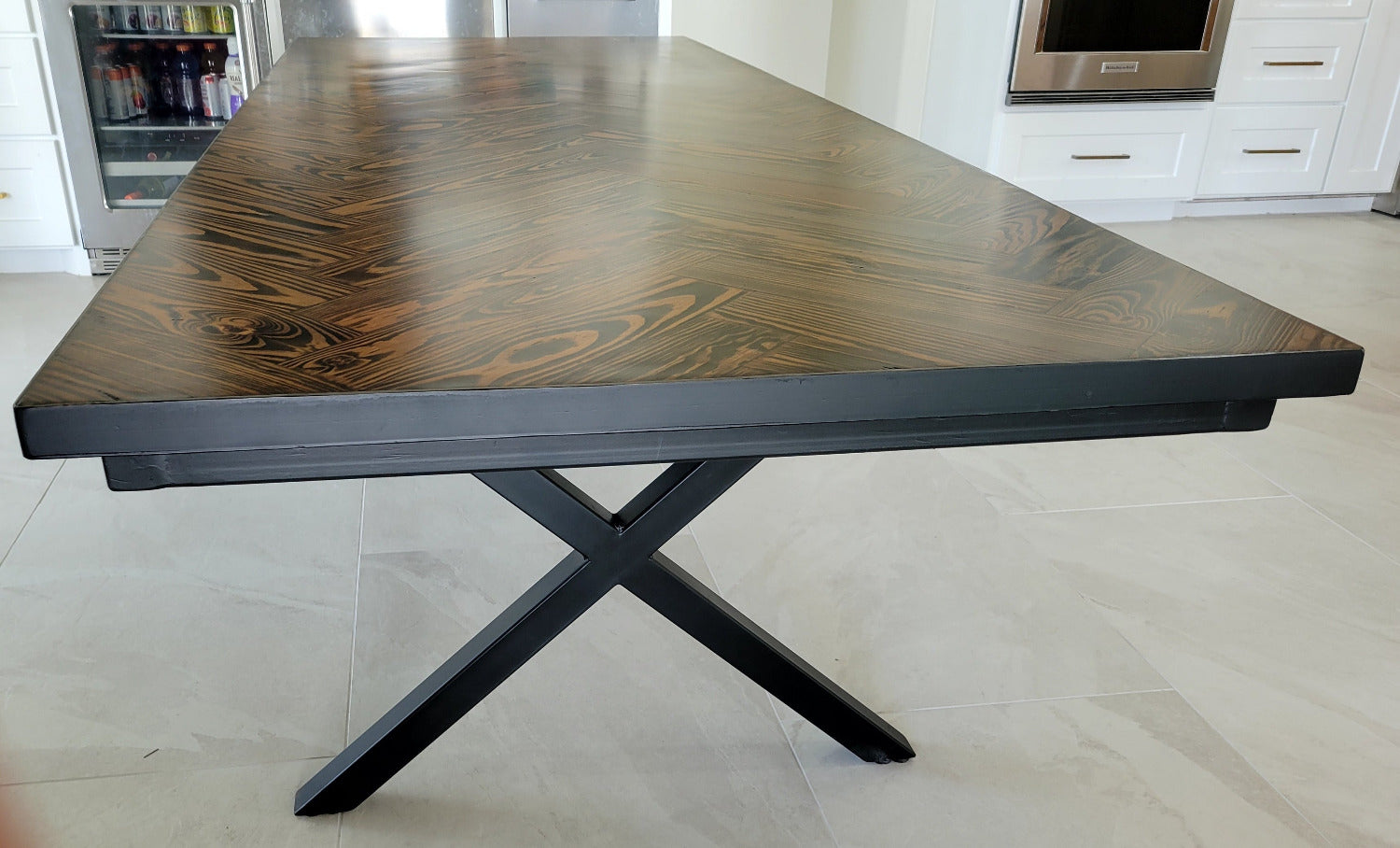 A rectangular long leaf pine dining table with a dark brown herringbone pattern top and black metal legs and metal sides shown in a home interior setting.