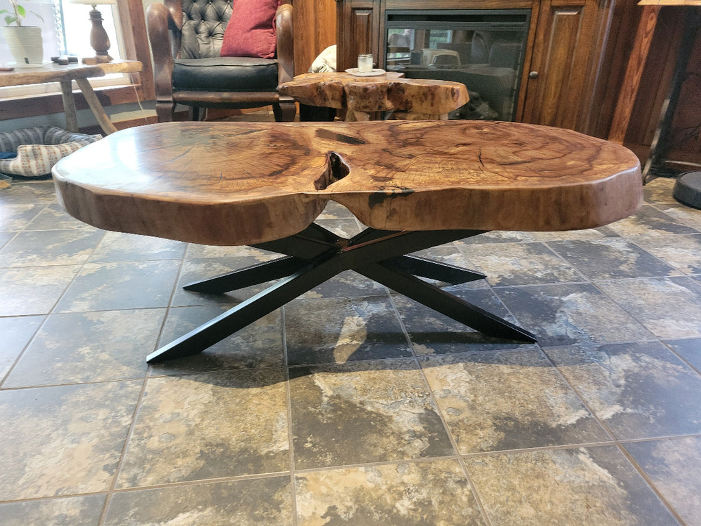 Wooden double tree coffee table with a natural, rustic design and black metal cross style legs in a living room setting.