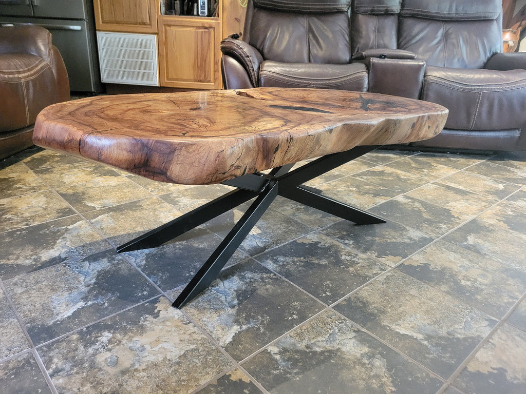 Wooden double tree coffee table with a natural, rustic design and black metal cross style legs in a living room setting.
