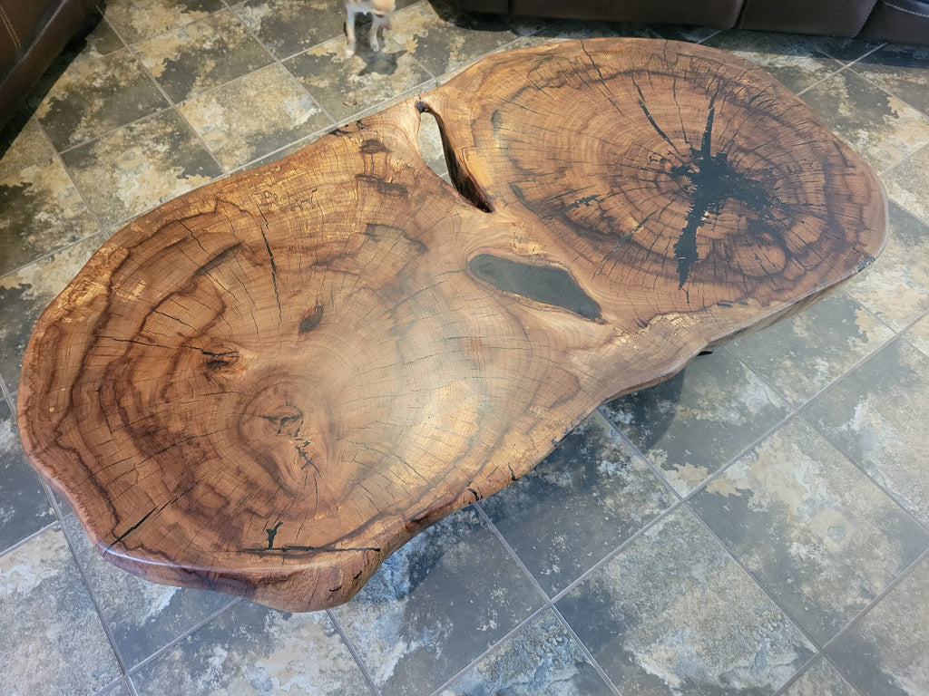 Wooden double tree coffee table with a natural, rustic design and black metal cross style legs in a living room setting.