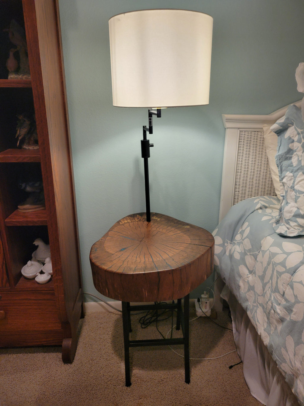 A rustic wooden table made from a live-edge tree slab with built in lamp stands and white drum lamp, black metal custom stand and turquoise epoxy fill