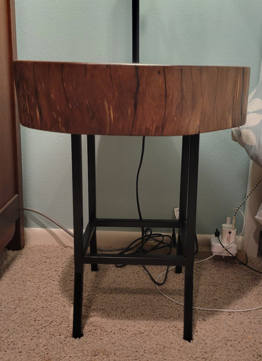 A rustic wooden table made from a live-edge tree slab with built in lamp stands and white drum lamp, black metal custom stand and turquoise epoxy fill