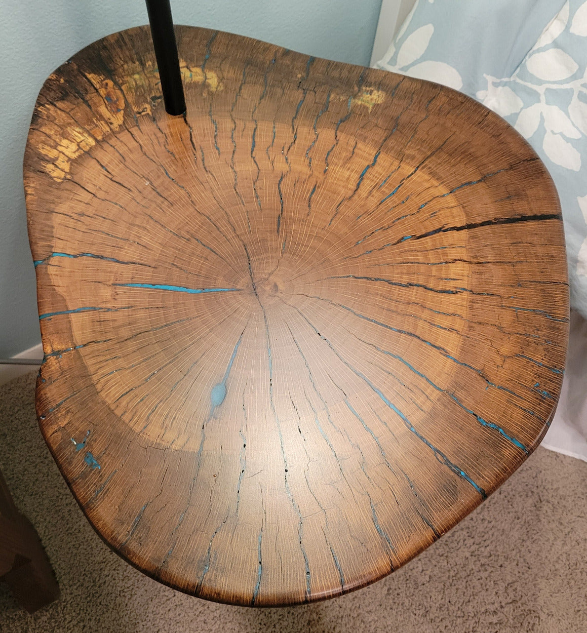 A rustic wooden table made from a live-edge tree slab with built in lamp stands and white drum lamp, black metal custom stand and turquoise epoxy fill