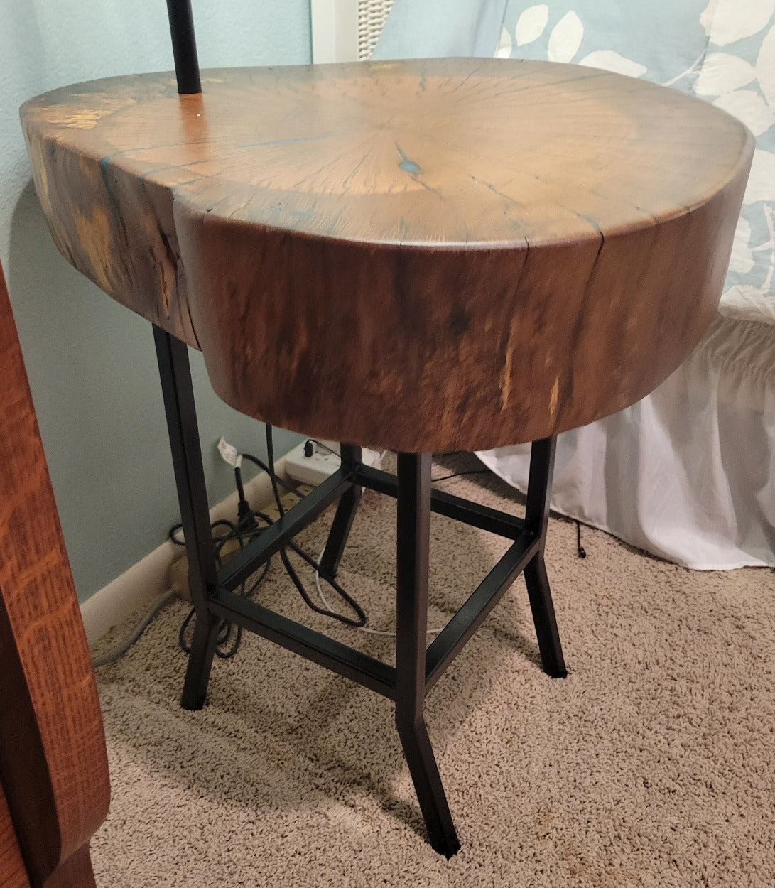 A rustic wooden table made from a live-edge tree slab with built in lamp stands and white drum lamp, black metal custom stand and turquoise epoxy fill