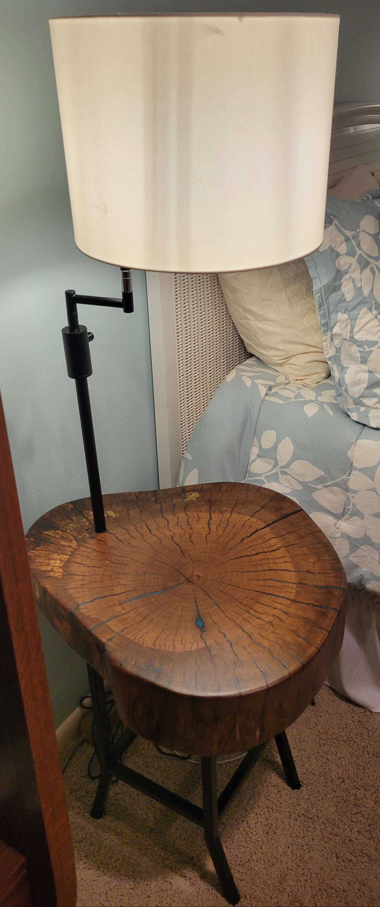 A rustic wooden table made from a live-edge tree slab with built in lamp stands and white drum lamp, black metal custom stand and turquoise epoxy fill