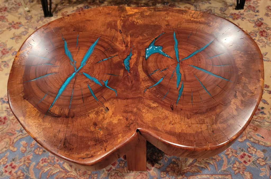 A rustic, organic-shaped wooden coffee table with a rich brown wood grain and bright turquoise blue resin inlay details, shown on a patterned oriental rug.