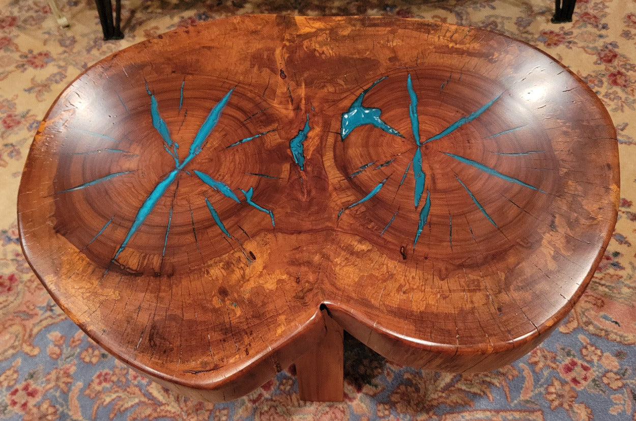 A rustic, organic-shaped wooden coffee table with a rich brown wood grain and bright turquoise blue resin inlay details, shown on a patterned oriental rug.