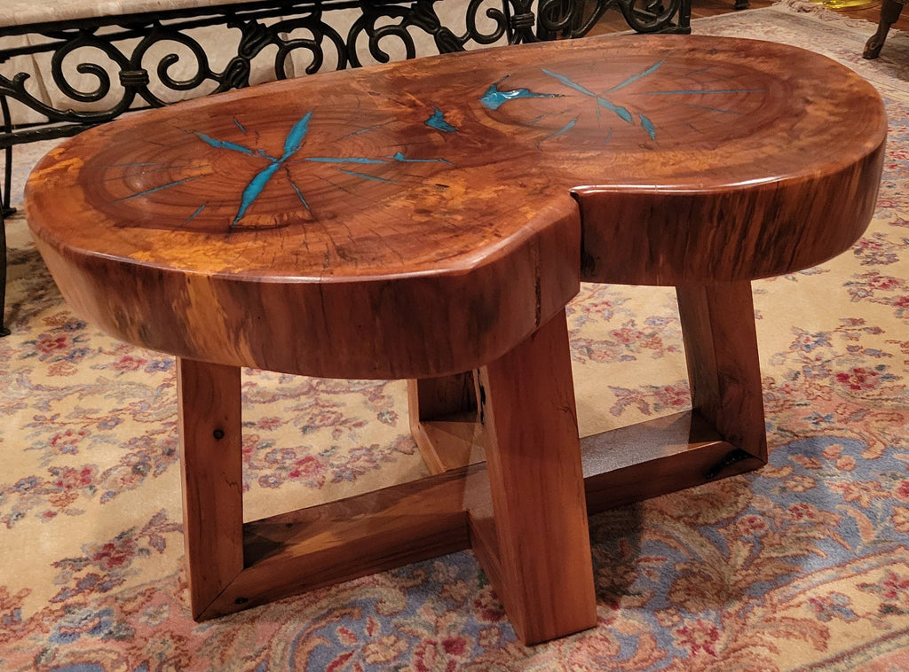 A rustic, organic-shaped wooden coffee table with a rich brown wood grain and bright turquoise blue resin inlay details, shown on a patterned oriental rug.