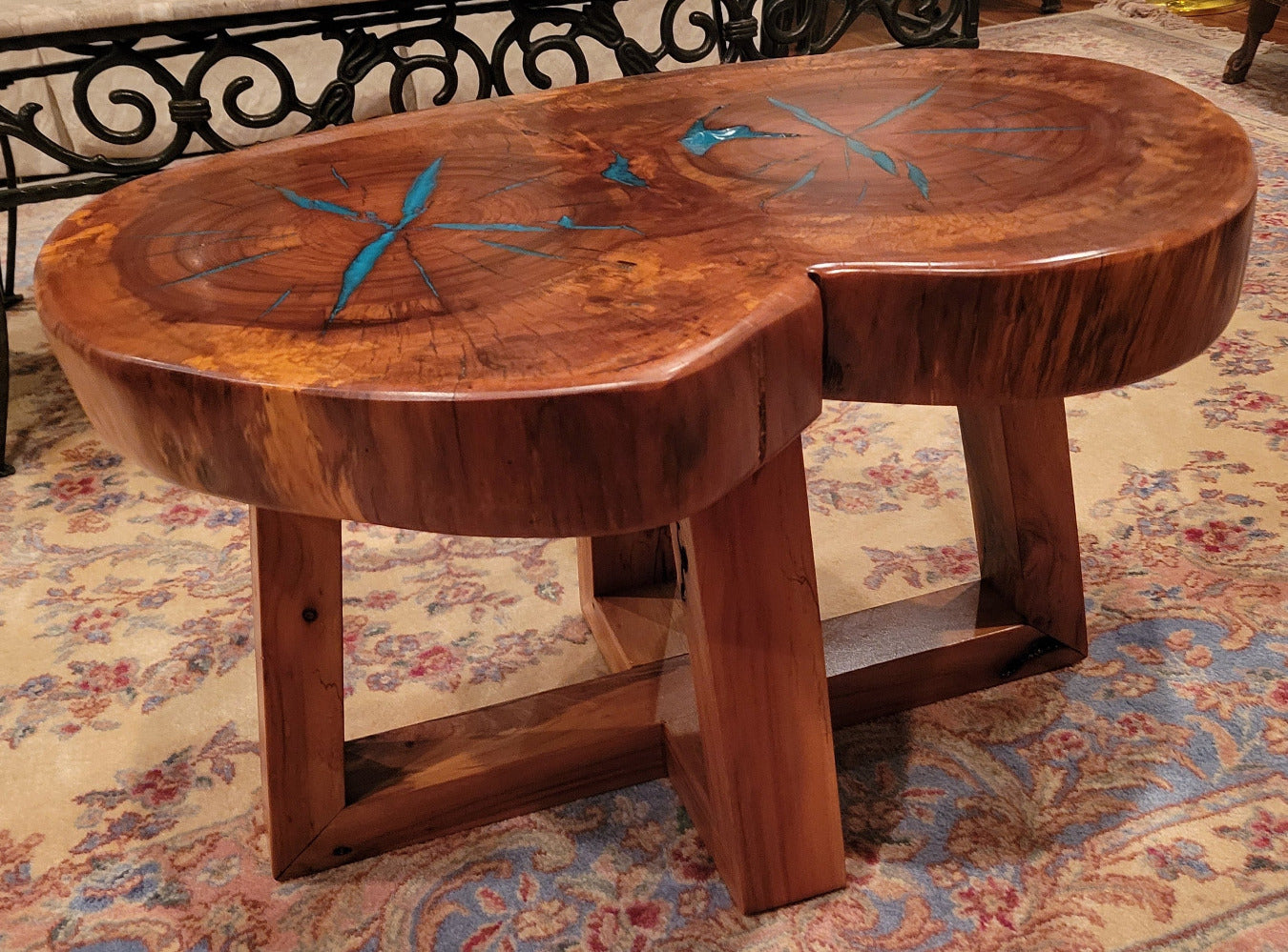 A rustic, organic-shaped wooden coffee table with a rich brown wood grain and bright turquoise blue resin inlay details, shown on a patterned oriental rug.