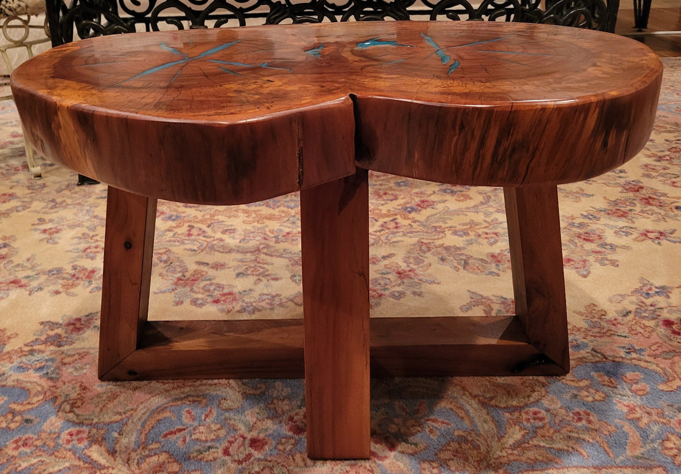 A rustic, organic-shaped wooden coffee table with a rich brown wood grain and bright turquoise blue resin inlay details, shown on a patterned oriental rug.