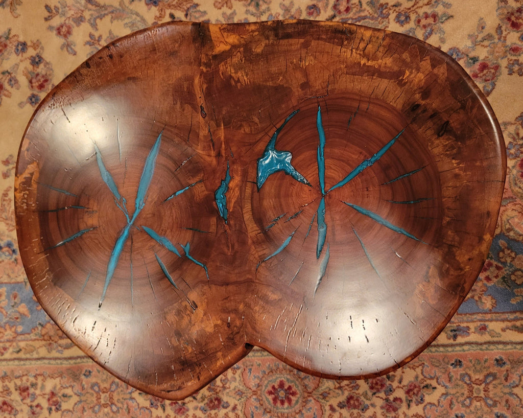 A rustic, organic-shaped wooden coffee table with a rich brown wood grain and bright turquoise blue resin inlay details, shown on a patterned oriental rug.