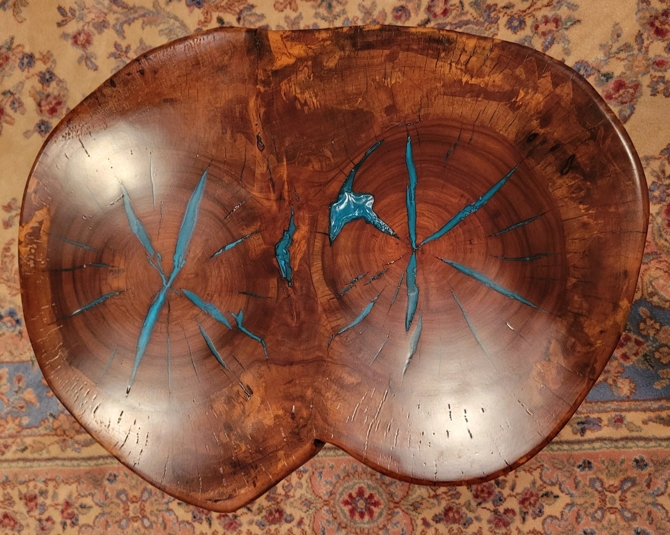 A rustic, organic-shaped wooden coffee table with a rich brown wood grain and bright turquoise blue resin inlay details, shown on a patterned oriental rug.