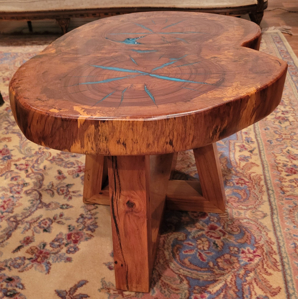 A rustic, organic-shaped wooden coffee table with a rich brown wood grain and bright turquoise blue resin inlay details, shown on a patterned oriental rug.
