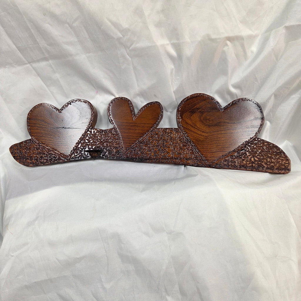 A rustic Bois D'Arc wooden plaque with three stacked heart-shaped tiers and hand carved, displayed on a wrinkled white fabric background.
