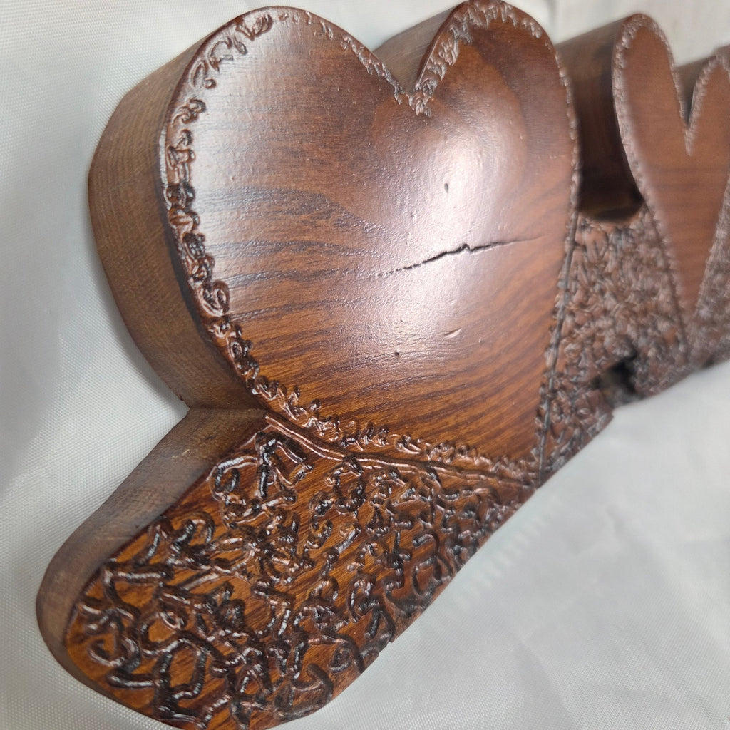 A rustic Bois D'Arc wooden plaque with three stacked heart-shaped tiers and hand carved, displayed on a wrinkled white fabric background.