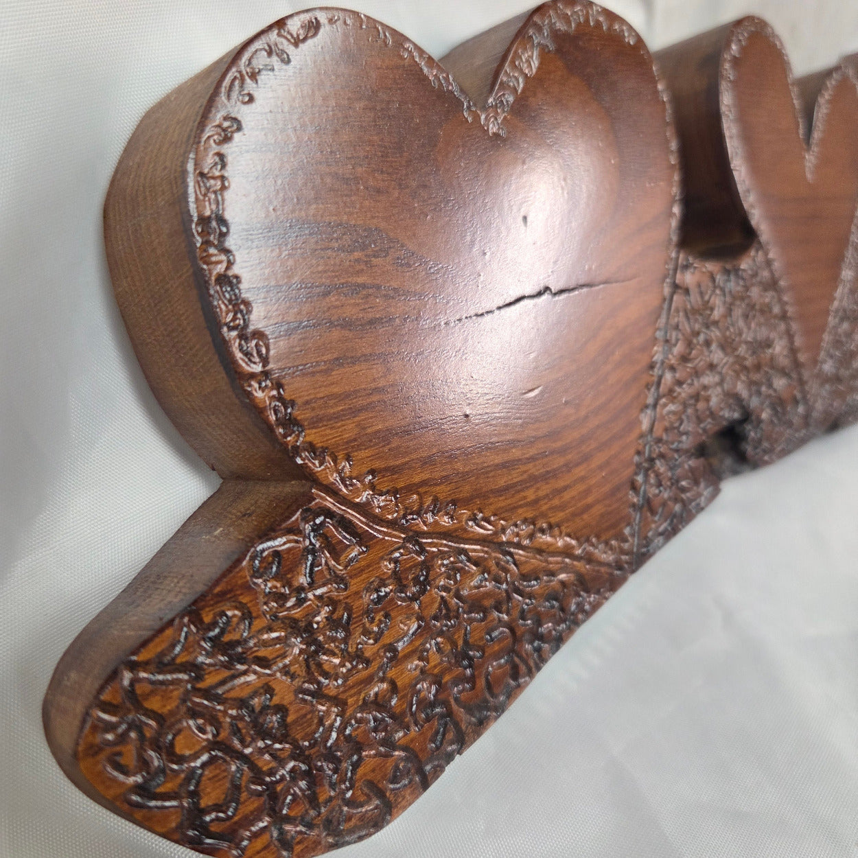 A rustic Bois D'Arc wooden plaque with three stacked heart-shaped tiers and hand carved, displayed on a wrinkled white fabric background.