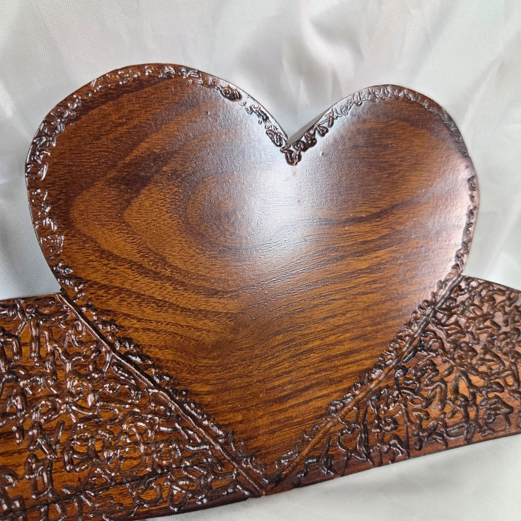 A rustic Bois D'Arc wooden plaque with three stacked heart-shaped tiers and hand carved, displayed on a wrinkled white fabric background.