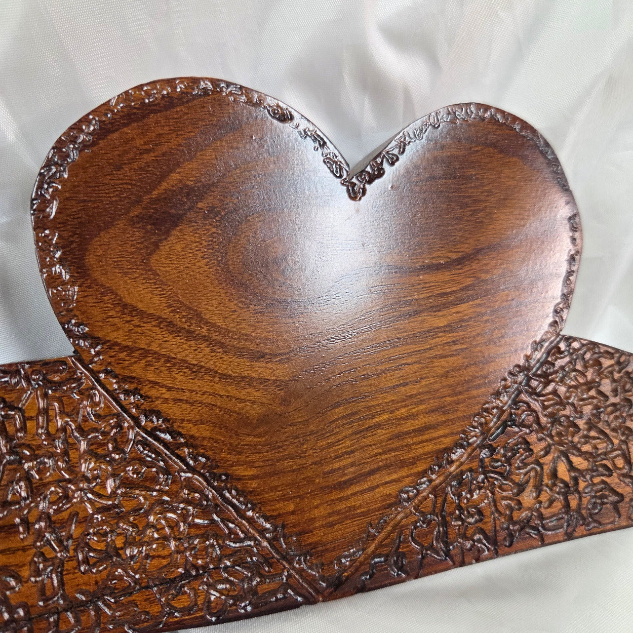 A rustic Bois D'Arc wooden plaque with three stacked heart-shaped tiers and hand carved, displayed on a wrinkled white fabric background.
