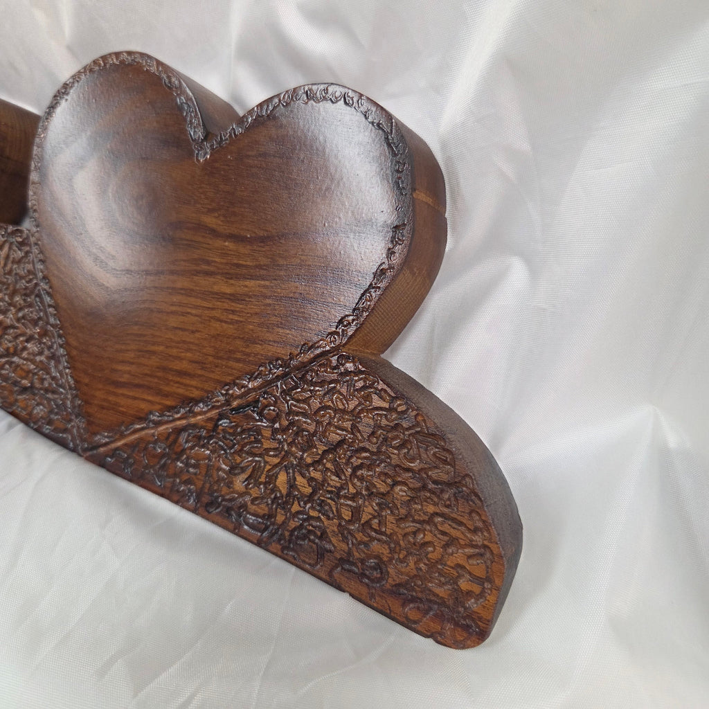 A rustic Bois D'Arc wooden plaque with three stacked heart-shaped tiers and hand carved, displayed on a wrinkled white fabric background.