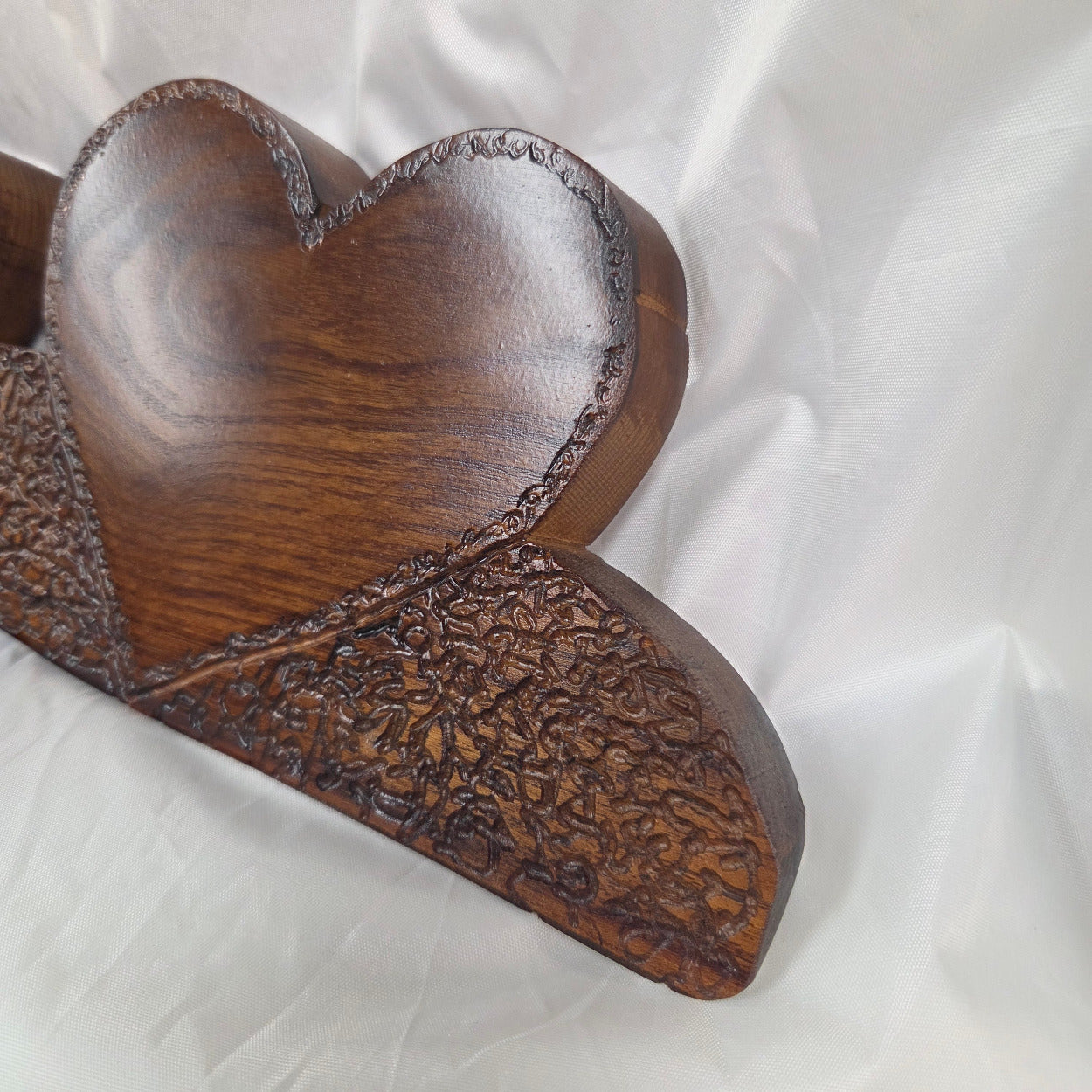 A rustic Bois D'Arc wooden plaque with three stacked heart-shaped tiers and hand carved, displayed on a wrinkled white fabric background.