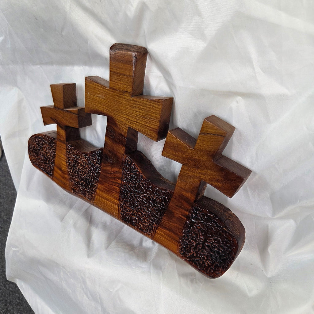 A Bois D'Arc decorative wall plaque featuring three stylized Christian crosses cut from a single slab, hand carved with burned finish sho sugi ban with natural grain 