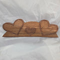 A handcrafted wooden plaque featuring three stacked heart shapes with engraved details, displayed on a wrinkled white fabric background.