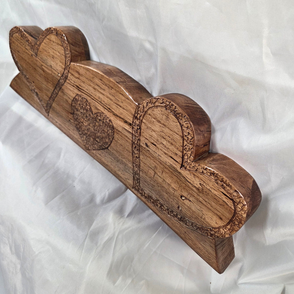 A decorative wooden wall shelf with three heart-shaped tiers, featuring carved floral details and a heart motif, displayed on a white fabric background.