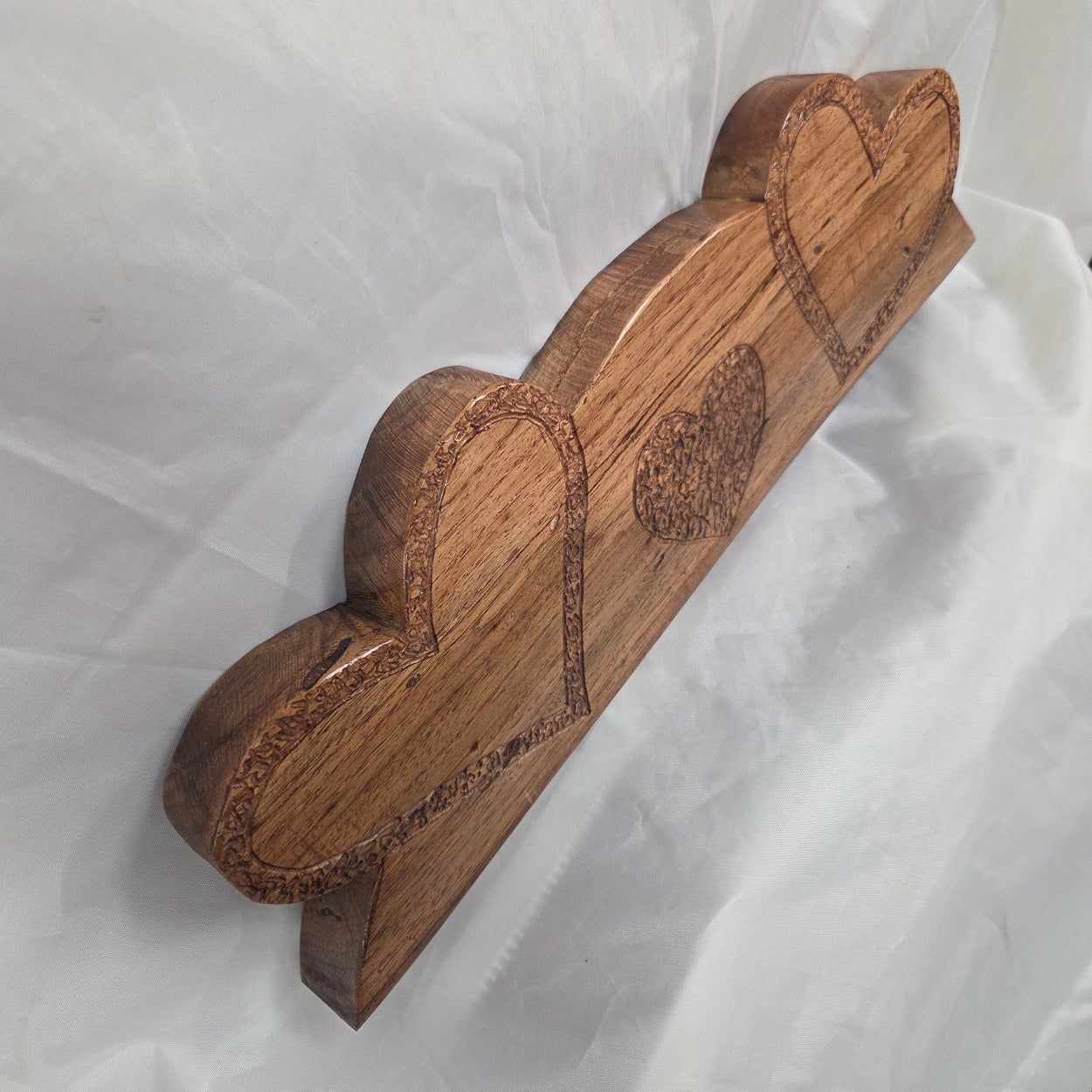 A handcrafted White Oak wooden plaque featuring three stacked heart shapes with engraved details, displayed on a wrinkled white fabric background.