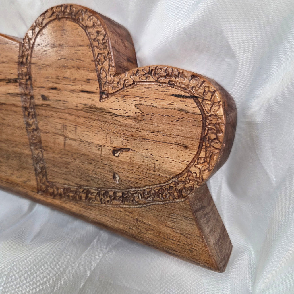 A heart-shaped wooden decorative object with carved floral border details, photographed against a white fabric background.