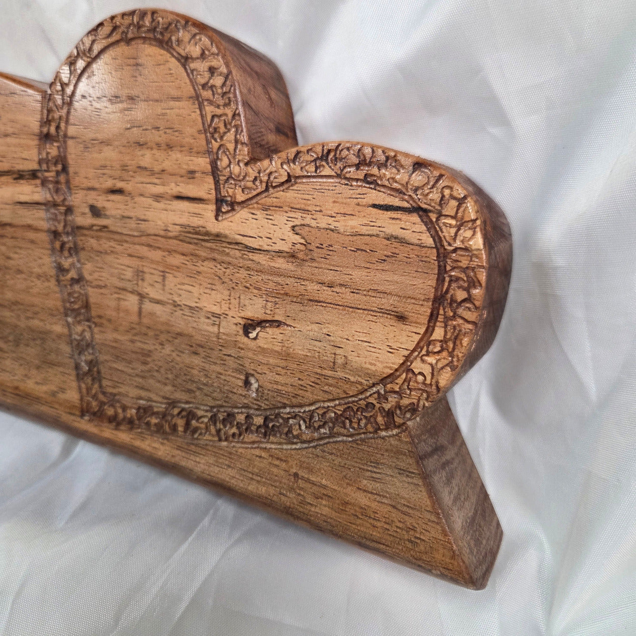 A heart-shaped wooden decorative object with carved floral border details, photographed against a white fabric background.