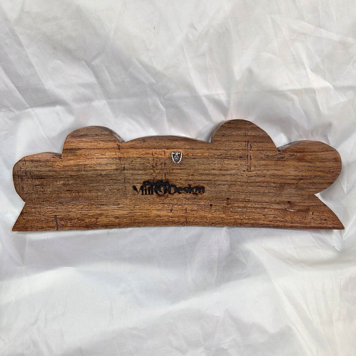 A rustic, handcrafted wooden plaque with a scalloped edge and a dark engraved brand name, displayed on a crumpled white background.
