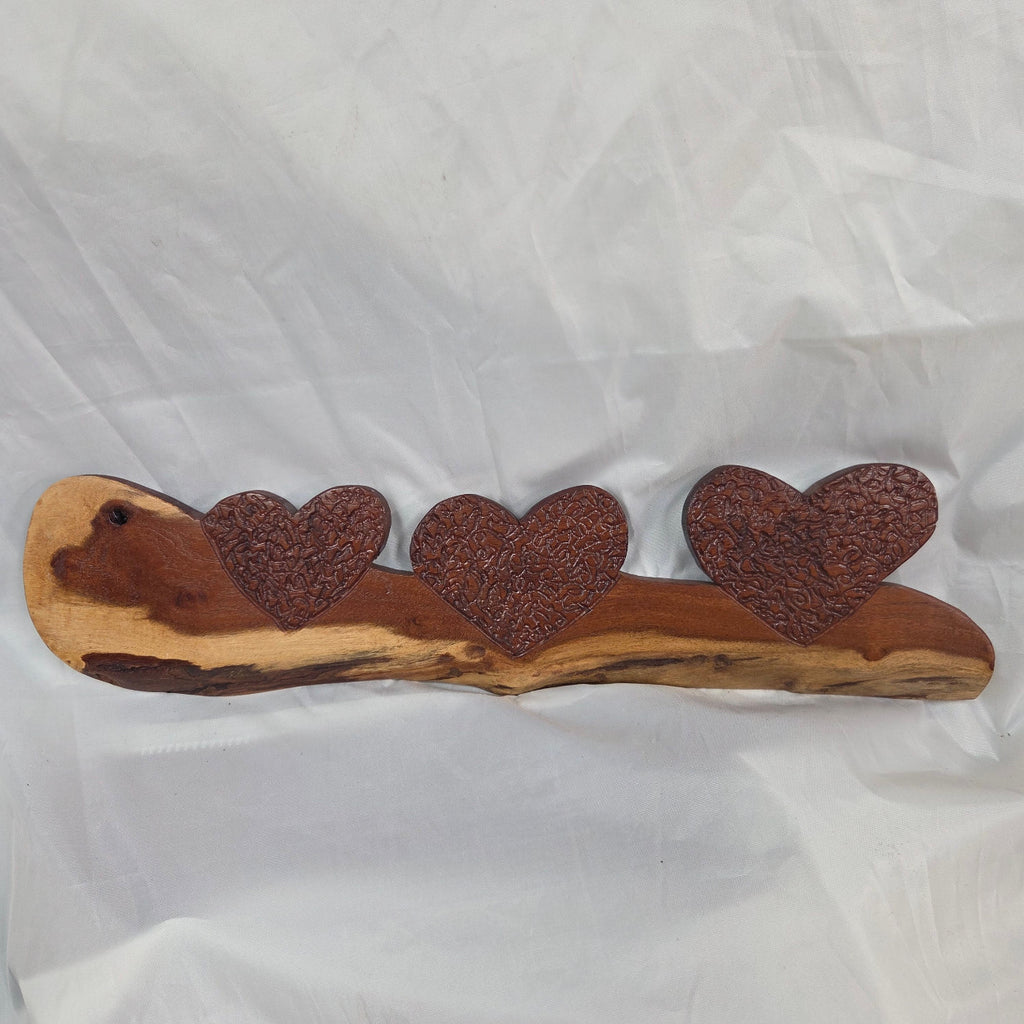 A rustic wooden decorative plaque featuring three hand carved hearts made from a single mesquite slab