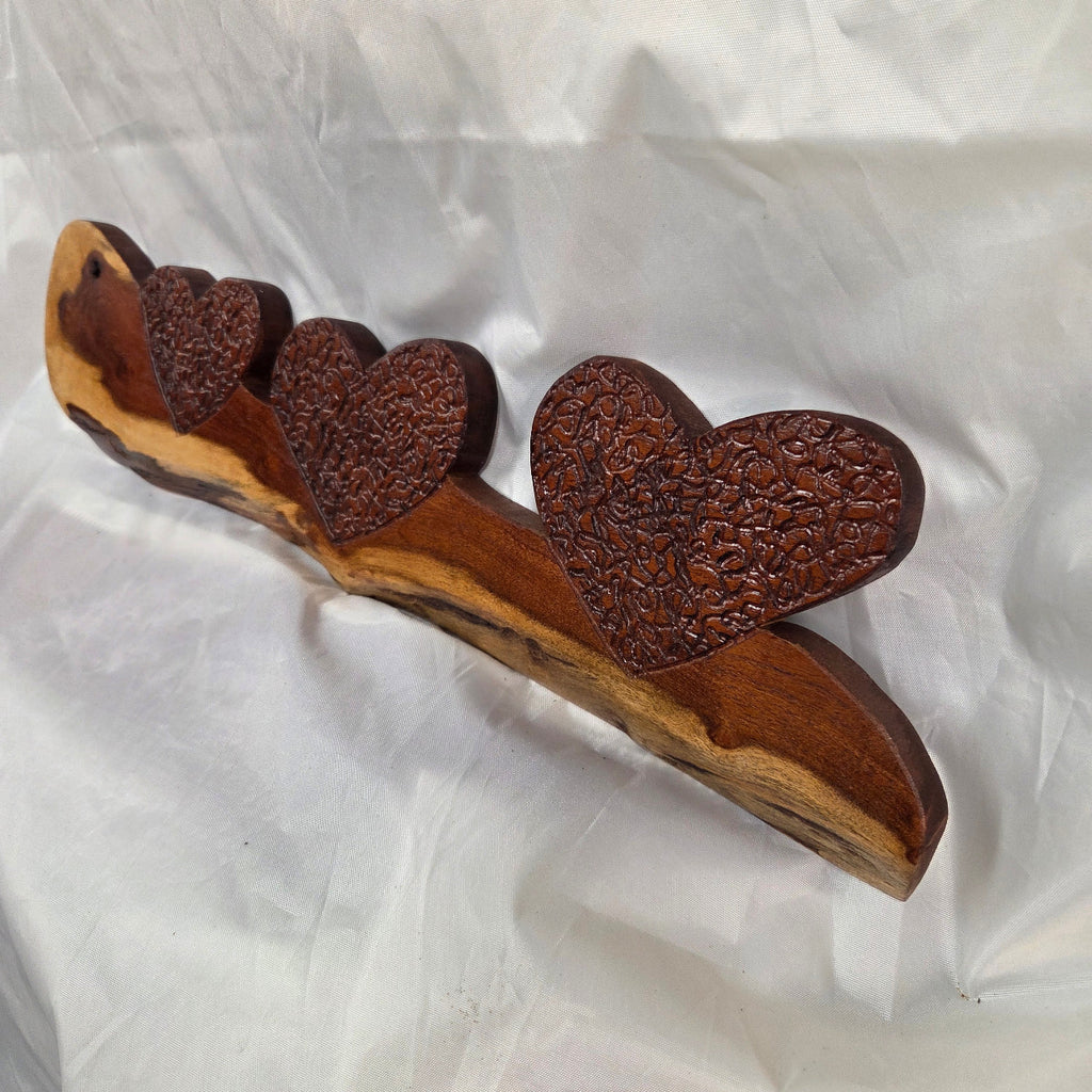 A rustic wooden decorative plaque featuring three hand carved hearts made from a single mesquite slab