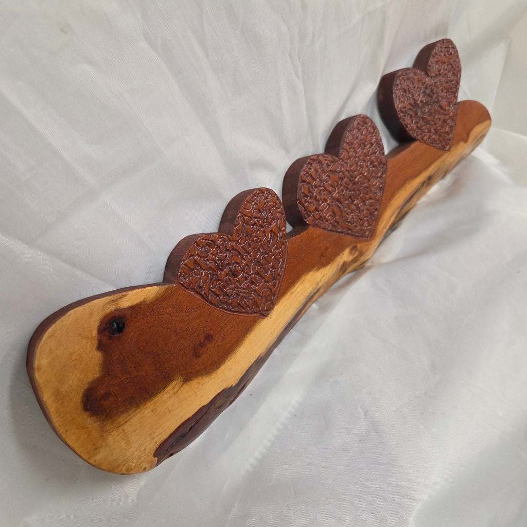 A rustic wooden decorative plaque featuring three hand carved hearts made from a single mesquite slab