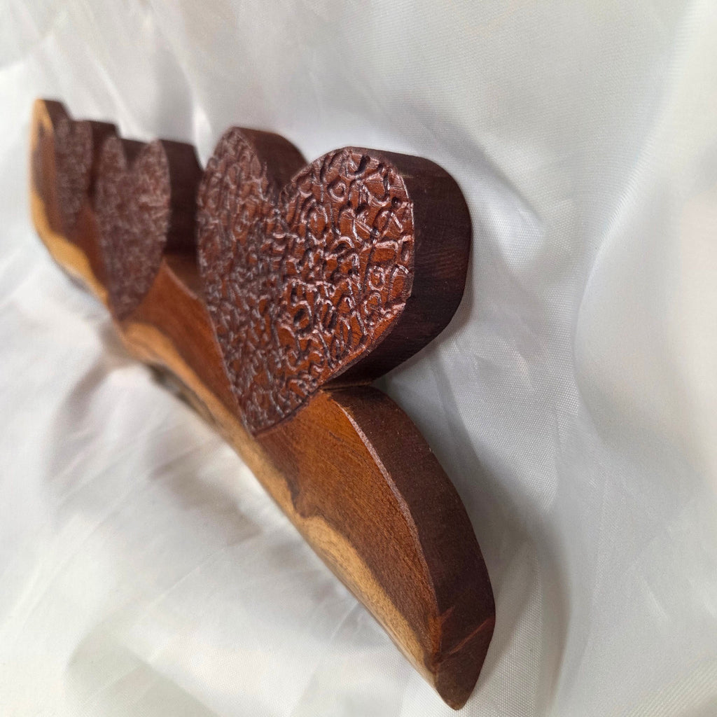 A rustic wooden decorative plaque featuring three hand carved hearts made from a single mesquite slab