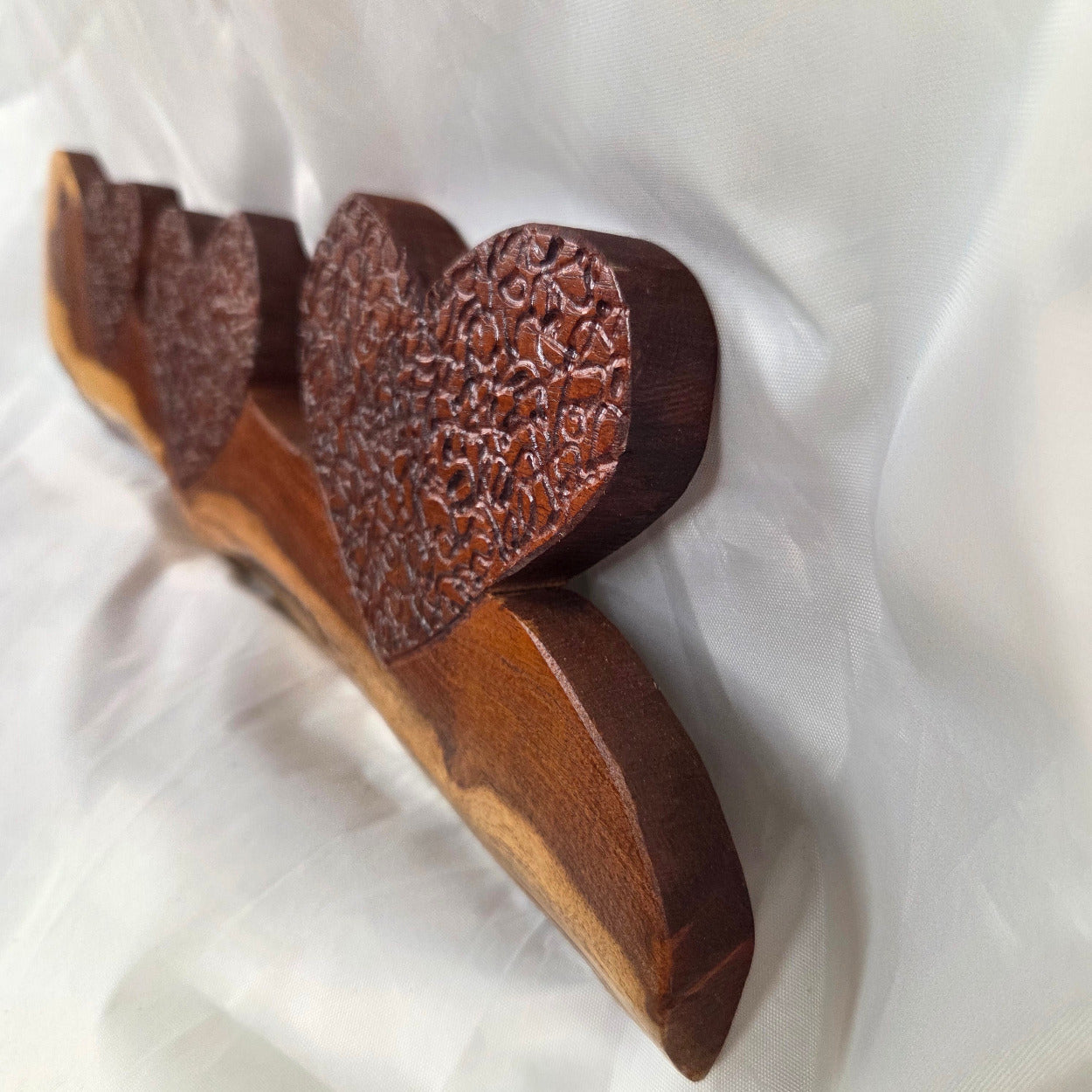 A rustic wooden decorative plaque featuring three hand carved hearts made from a single mesquite slab